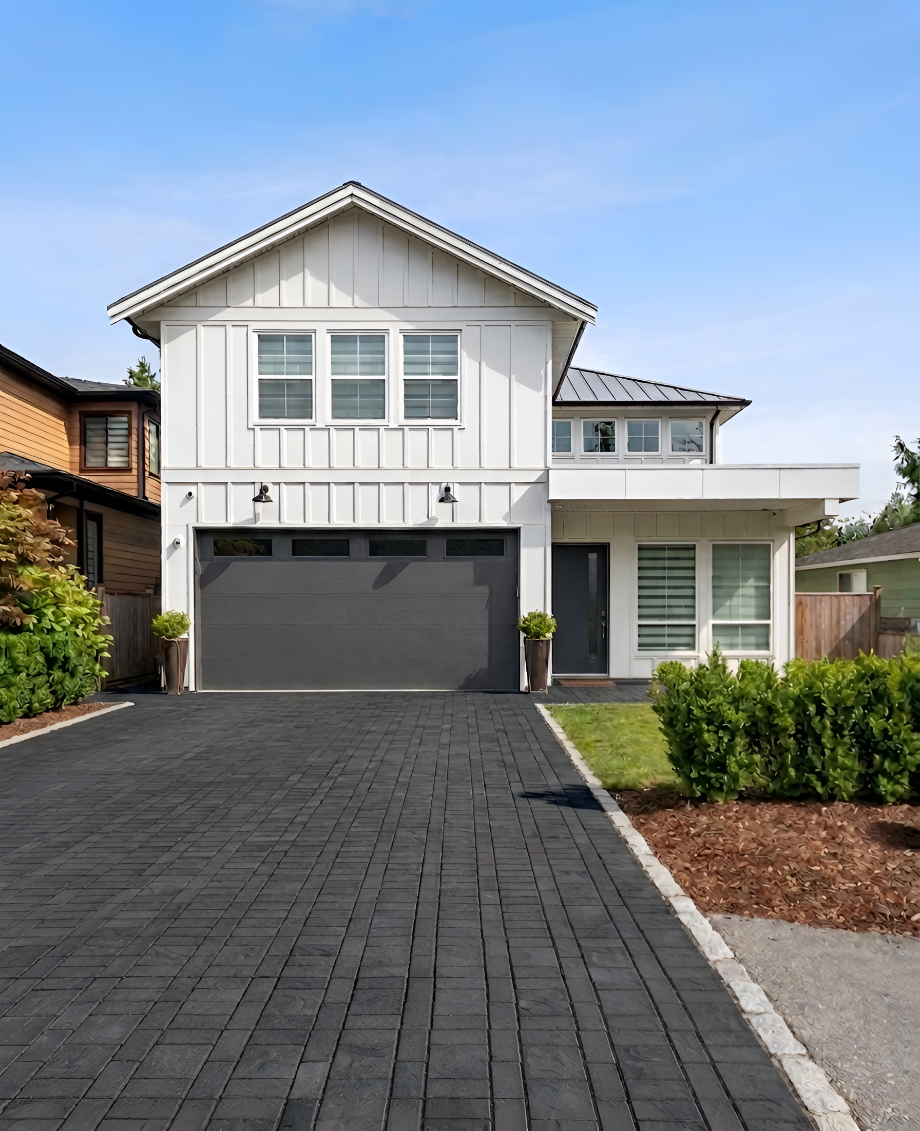 White board-and-batten modern farmhouse with dark garage door and paver driveway